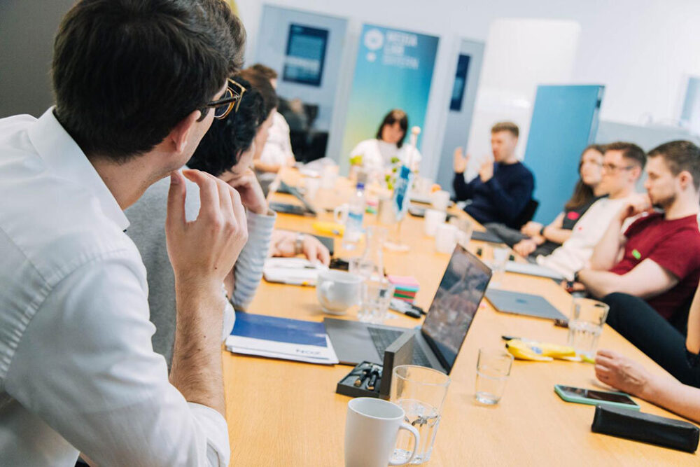 Eine Gruppe diverser Menschen, die an einem langen Tisch sitzen und ein Thema besprechen.