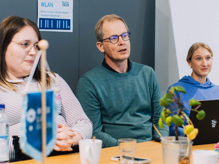 Zwei Frauen und ein Mann sitzen an einem Konferenztisch und nehmen an einer Diskussion teil.