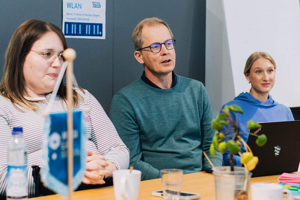 Zwei Frauen und ein Mann sitzen an einem Konferenztisch und nehmen an einer Diskussion teil.