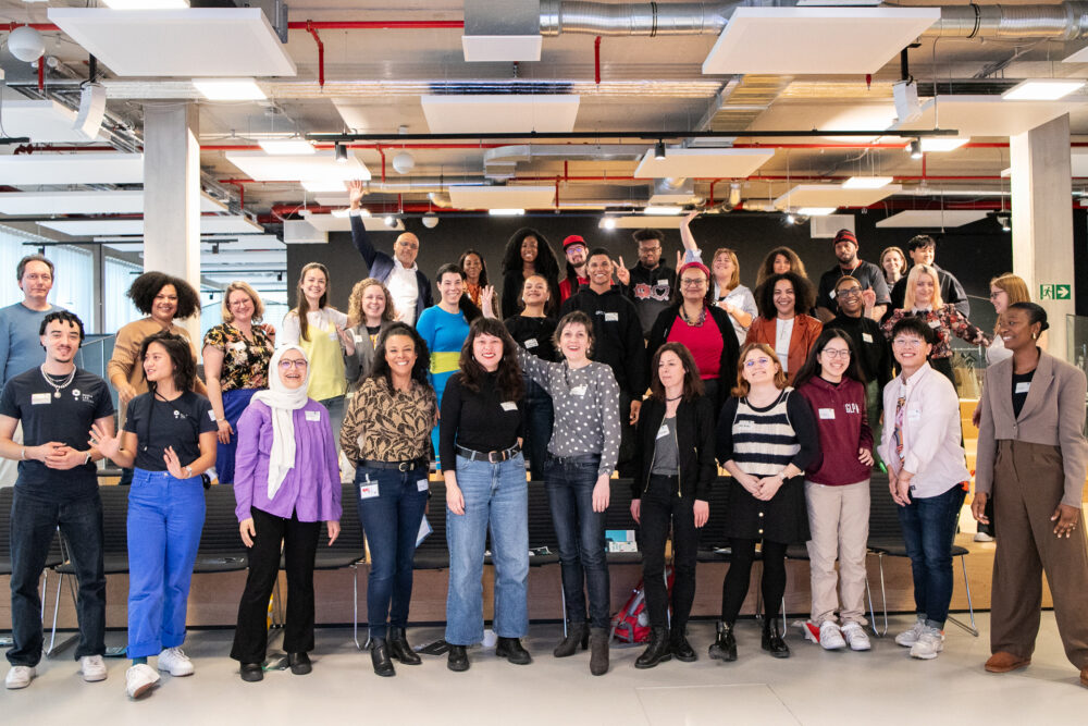 Eine große Gruppe von Menschen mit Migrationshintergrund steht auf einer Bühne.