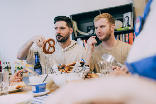 Zwei junge Männer sitzen an einem Tisch und essen Brezeln.