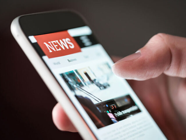 Person hält ein Smartphone in der Hand und liest Nachrichten auf einer News-Website