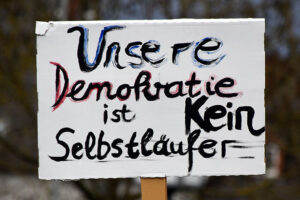 Schild auf einer Demo mit Schriftzug „Unsere Demokratie ist kein Selbstläufer“